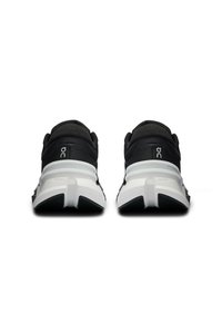 Black athletic shoes featuring a textured upper, white midsole, and rubber outsole with flexible traction. Notable logo on heel.