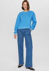 Mėlynas megztinis su apvalia iškirpte, derinamas su aukštu liemeniu plačiais mėlynais džinsais ir juodais balerinais. Paprastas dizainas su laisvu siluetu.