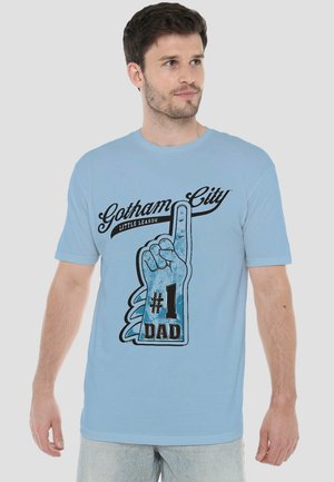 Man wearing light blue T-shirt with graphic of foam finger and text "Gotham City Little League #1 Dad," looking slightly right.
