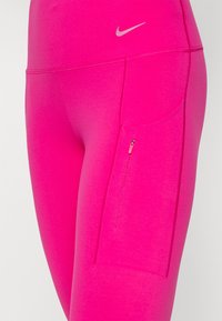 Roze sportlegging met een zijrits zak, een gladde textuur, een hoge tailleband en een klein zilveren logo aan de voorkant.