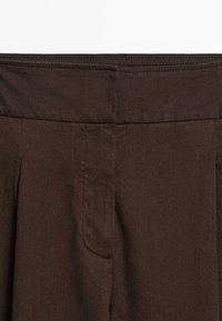 Close-up van een bruine stof die de gedetailleerde stiksels en een tailleband met een verticale naad in het midden toont.