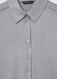 Camicia grigia in tessuto seta, con colletto classico, dotata di chiusura con bottoni frontale e sei bottoni visibili, texture liscia senza fantasie.