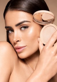 Poudre compacte avec un boîtier beige, équipée d'un miroir. Texture lisse et réfléchissante sur la peau, pommette mise en valeur, sourcils définis.