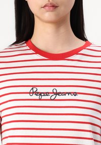 Rød og hvit stripete T-skjorte, laget av bomull, med rund hals og en svart "Pepe Jeans"-logo på forsiden. Korte ermer.