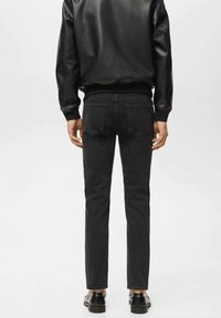 Schwarze Lederjacke mit geripptem Kragen, kombiniert mit schlanken schwarzen Jeans mit Gesäßtaschen. Glatte Textur mit minimalen Details.