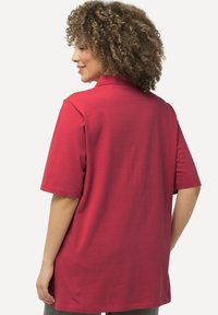 Polo shirt rosso a maniche corte con una texture morbida e colletto standard, caratterizzato da una vestibilità comoda e spacchi laterali per facilitare i movimenti.