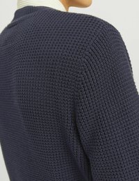 Marinblåstickad tröja med en strukturerad yta, ribbade detaljer, rund halsringning och sänka axelsömmar, delvis visad bakifrån.