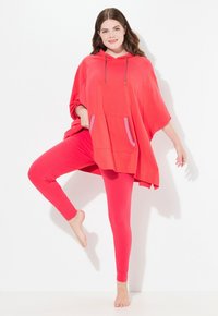 Poncho rosso con cappuccio, dotato di tasca frontale e accenti a righe, abbinato a leggings rossi coordinati. Tessuto morbido con una vestibilità ampia e confortevole.