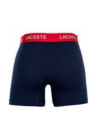 Boxer briefs blu navy con una vita rossa con il testo bianco "LACOSTE". Realizzati in un tessuto morbido e elasticizzato con una texture liscia.