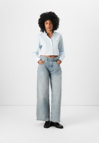 Light blue cropped button-up shirt, wide-leg light denim jeans, and black shoes, with a smooth texture and subtle stitching details.