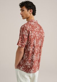 Chemise à manches courtes en rouille avec imprimé floral blanc. Dotée d'un col camp et d'une coupe décontractée, fabriquée en tissu léger.