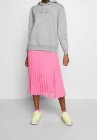 Felpa grigia con cappuccio e lacci, abbinata a una gonna plissettata rosa e sneakers neon con dettagli rosa. Combinazione di outfit semplice e sportiva.