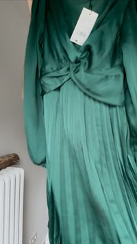Grünes plissiertes Kleid aus Satin, mit einem geknoteten Taillendetail und langen Ärmeln. Mit einem angehängten Produktetikett.