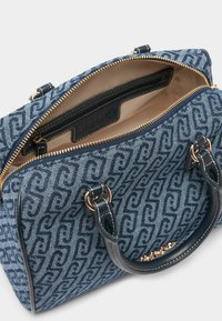 Blaue Denim-Handtasche mit Logo-Druck. Goldene Reißverschlüsse, cremefarbiger Innenraum. Zwei kurze Griffe mit Marineleder-Akzenten. Glatte Textur und strukturierte Form.
