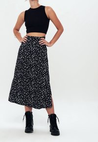 Top corto negro de canalé combinado con una falda larga y fluida negra con flores blancas y una abertura lateral, complementado con botas negras con cordones.