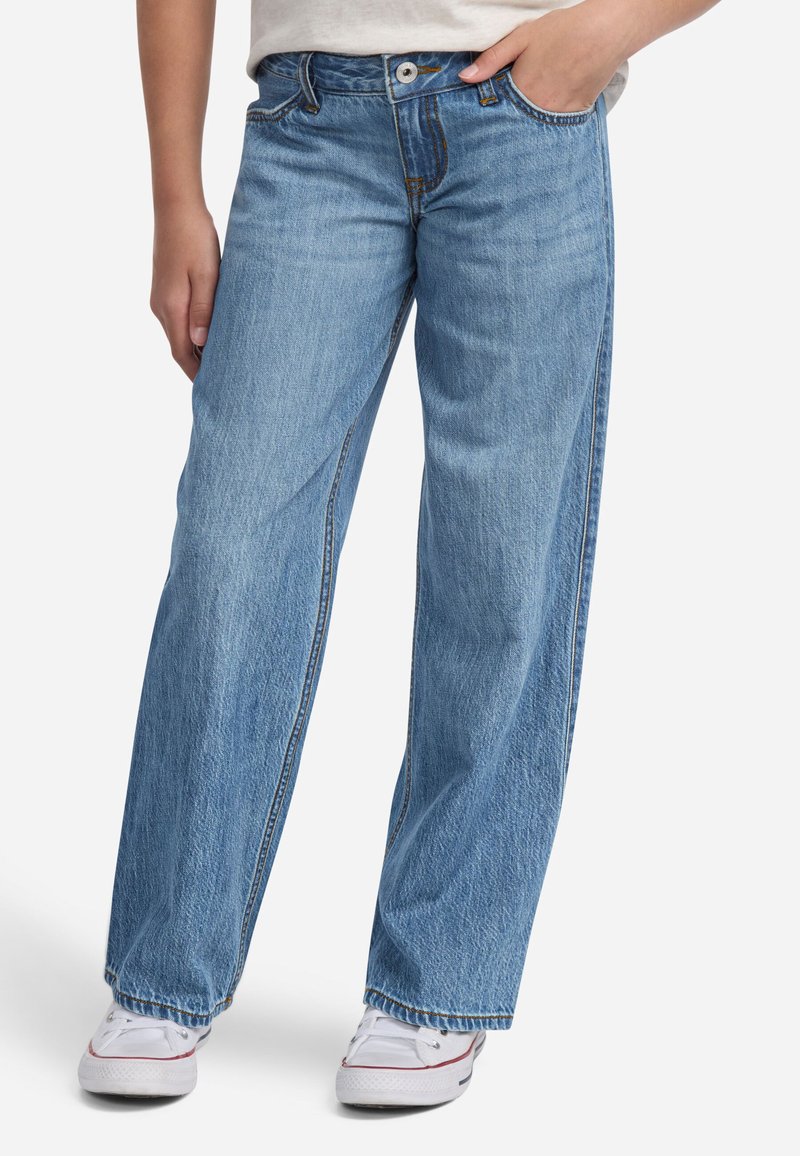 Jeans in denim blu chiaro con vestibilità comoda, cuciture a vista, passanti per la cintura e tasche frontali. Abbinati a scarpe in tela bianche.