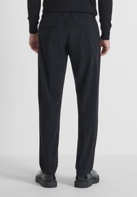 Zwarte corduroybroek met een relaxed fit, elastische tailleband en twee achterzakken. Draag het met zwarte schoenen, tegen een effen achtergrond.