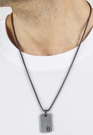 Silberner Hundemarkenanhänger mit Kompass-Emblem an einer Boxkettengliederkette, getragen über einem weißen T-Shirt mit Rundhalsausschnitt.