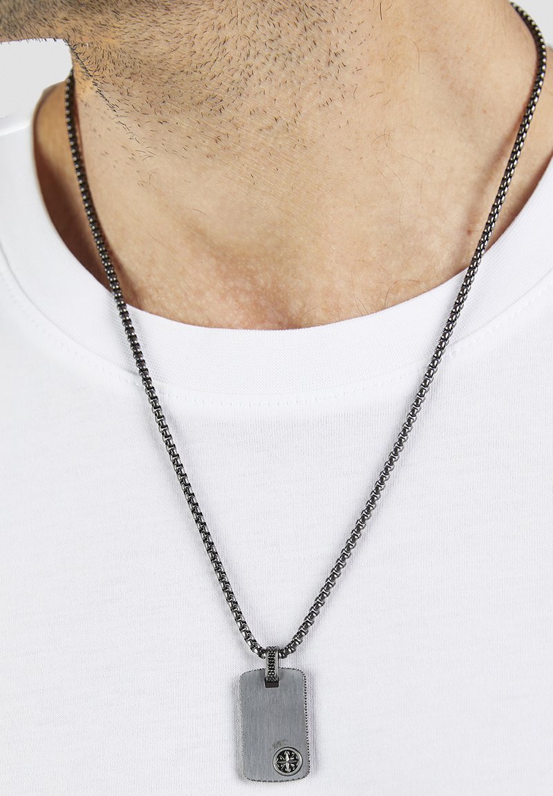 Pendentif plaquette militaire en argent avec un emblème de boussole sur une chaîne à maillons, porté sur un t-shirt blanc à col rond.