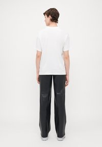 Vit bomullst-shirt med korta ärmar, kombinerad med svarta, högmidjade byxor i imiterat läder. Modellen sedd bakifrån.