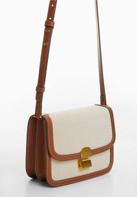 Rektangulær beige crossbody taske med brunt læderkant, justerbar rem og guldtonet lukning.