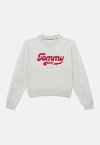 Gaišpelēka adīta džemperis ar sarkano „Tommy Class of 1985” tekstu priekšpusē un mazo Tommy Hilfiger logo kreisajā piedūrē.