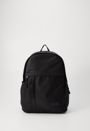 Zwarte nylon rugzak met een gebogen bovenkant, voorzak met rits en een subtiele logopatch. Voorzien van verstelbare schouderbanden en een gestructureerde afwerking.