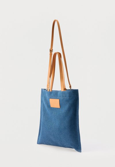 Μπλε υφασμάτινη τσάντα ώμου με δύο κοντές και μία μακριά χειρολαβή από ταμπά δέρμα, με ένα μικρό πάπλωμα από ταμπά δέρμα στο μπροστινό μέρος.