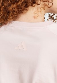 Svetloružový sweatshirt s rebrovým golierom a vyvýšeným, tónovým logom adidas s tromi pruhmi na chrbte. Mäkký tkaninový vzhľad.