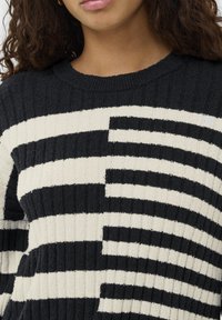 Gestrickter Pullover mit schwarz-weiß gestreiftem Muster, gerippter Struktur und rundem Ausschnitt. Weicher Stoff mit kontrastierenden Farbfeldern.