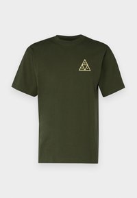 T-shirt en coton vert olive avec des manches courtes et un col rond. Présente un graphique triangulaire jaune avec des lettres sur la poitrine gauche.