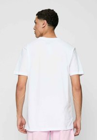 Hvid kortærmet t-shirt med rund hals, der har et enkelt design og afslappet pasform, vist fra bagsiden. Materialet ser blødt og glat ud.