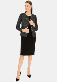 Czarna marynarka z tweedu z kolorowymi włóknami, okrągłym dekoltem i złotymi guzikami, noszona na dopasowanej czarnej sukience i zestawiona z czarnymi szpilkami.