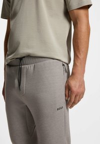 Graue Jogginghosen aus Baumwolle mit elastischem Bund und Tunnelzug, ausgestattet mit Seitentaschen und einem schwarzen "BOSS"-Logo am linken Oberschenkel.