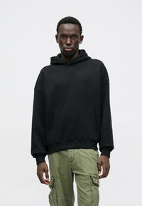 Μαύρη φούτερ μπλούζα με κουκούλα και τσέπη καγκουρό, φτιαγμένη από μαλακό βαμβάκι, διαθέτει άνετη εφαρμογή και πλεκτές μανσέτες, συνδυασμένη με ελκυστικά cargo παντελόνια σε ελιά.