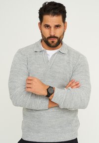 Grau gestreifter Pullover mit kragenförmigem Ausschnitt, weichem Stoff und langen Ärmeln. Mit einer schwarzen Uhr am Handgelenk accessorisiert.