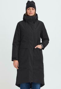 Svart vattentät jacka med huva, frontknappslås, två sidofickor och justerbara dragsnören. Slät textur och knälång design.