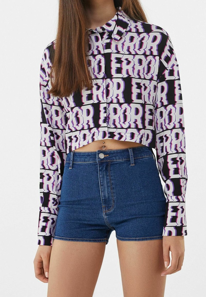 Chemise à manches longues raccourcie en noir et blanc avec le texte violet "ERROR" ; associée à un short en jean taille haute dans un denim foncé.