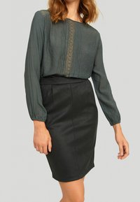 Černá tužková sukně v kombinaci s dlouhým rukávem z tečkované teal blůzy, která má vertikální záhyby a elastické manžety.