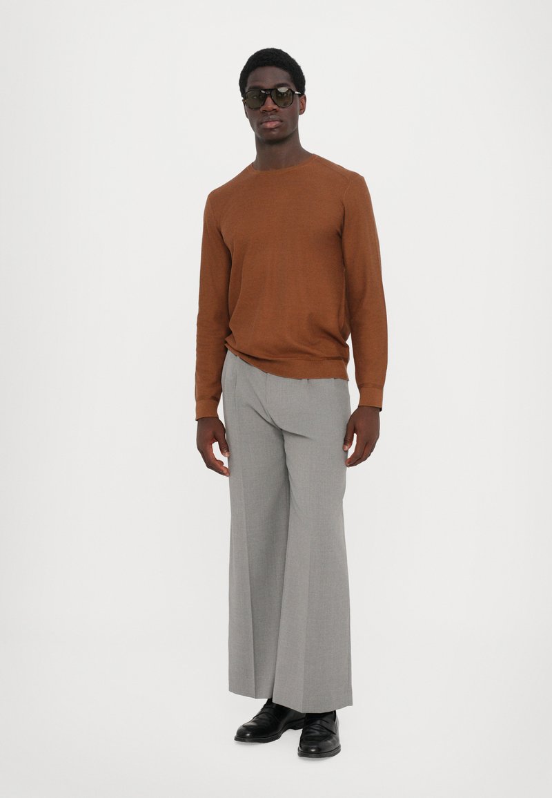 Brun långärmad tröja, grå vida byxor, svarta skor och solglasögon. Slätt tyg och avslappnad passform med en minimalistisk design.