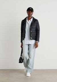 Black quilted jacket, light blue striped shirt, loose light denim pants with side embroidery, white sneakers, and a black handbag. Cap worn.