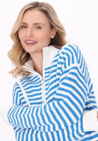 Blå och vit randig tröja med hög krage och dragkedja, med ribbade ärmslut och ett strukturerat stickat mönster.