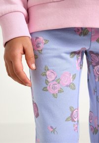 Ljusblå leggings med ett heltäckande blommönster av rosa rosor och gröna blad. En rosa ribbad muddarm syns delvis.