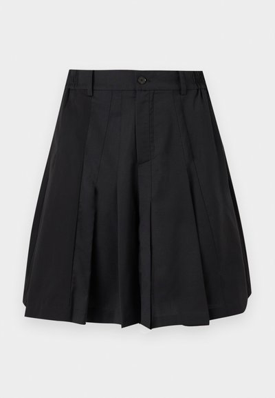 Μαύρη πλισέ φούστα μέχρι το γόνατο με κουμπιά μπροστά και θηλιές ζώνης στη λευκή επιφάνεια.