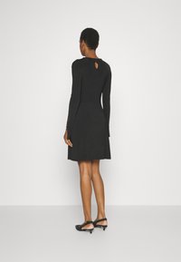 Robe longue noire à manches longues avec un corsage ajusté et une jupe évasée, dotée d'un détail en forme de clé au dos et d'un tissu texturé.