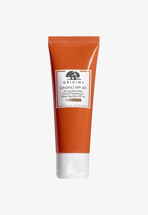 Oranje tube met een witte dop, gelabeld "Origins GINZING SPF 40," met zwarte tekst en een boomlogo. Compact, plastic ontwerp voor gemakkelijke hantering.