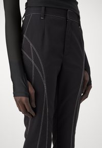 Pantalon noir avec des coutures contrastantes blanches, arborant une coupe slim et des accents latéraux. Fabriqué en un tissu doux et texturé.