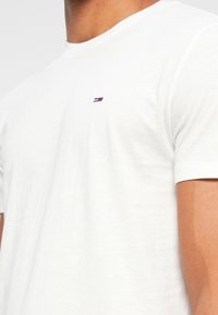 Λευκό βαμβακερό t-shirt με στρογγυλή λαιμόκοψη, κοντά μανίκια και ένα μικρό, κεντημένο λογότυπο με κόκκινες, μπλε και �λευκές ρίγες στο στήθος.