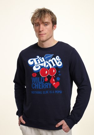 Granatowy sweatshirt z graficznym wzorem przedstawiającym czerwone wiśnie, niebieski tekst i liść. Miękki materiał, okrągły dekolt i długie rękawy.
