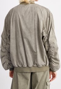 Olive green bomber jacket featuring gathered sleeves, ribbed cuffs and hem, made of a soft, textured fabric with a relaxed fit.